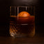 Glass of whiskey with a cherry whiskey sphere inside.