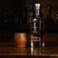 A hand holding a cherry whiskey tumbler glass with a whiskey bottle to the right