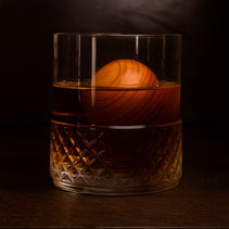 Glass of whiskey with a cherry whiskey sphere inside.