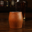 A hand holding a cherry whiskey tumbler glass with a whiskey bottle to the right